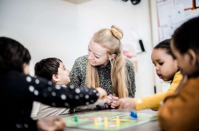 Kvindelig pædagog med børn, der spiller Ludo
